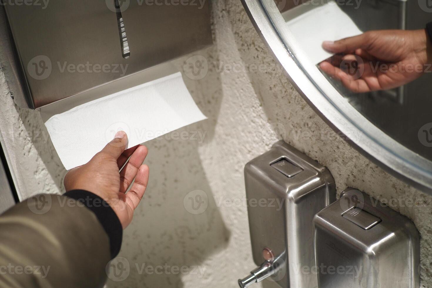 Hand Using Paper Towel Dispenser in a Hygienic Public Restroom with Clean White Tiles photo