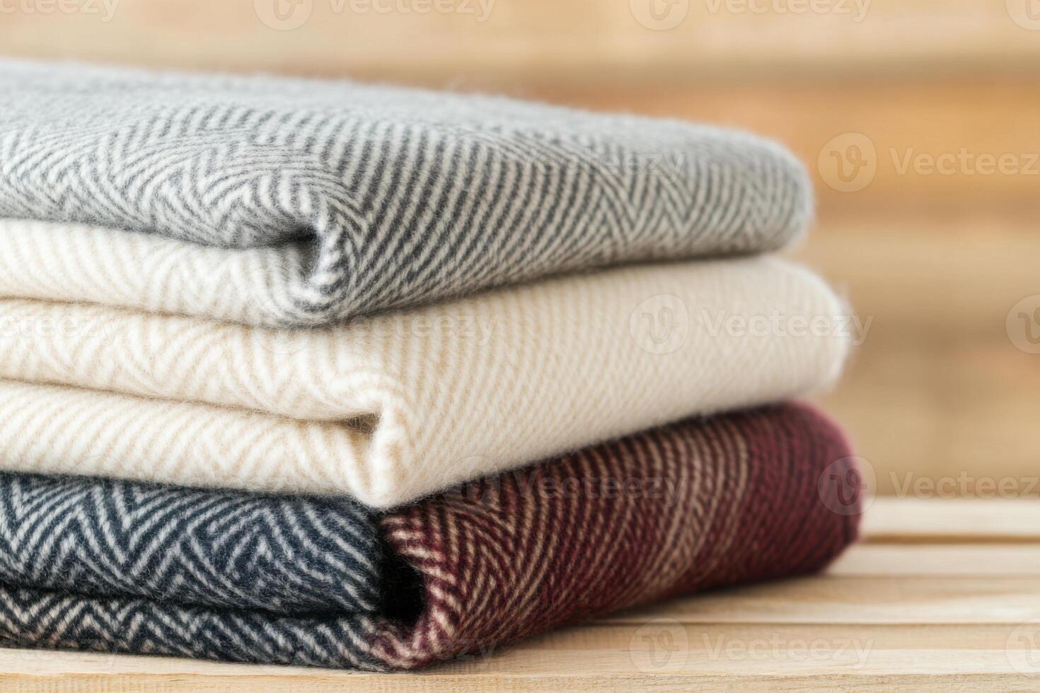 Cozy woolen blankets stacked neatly on a rustic wooden bench for warmth and comfort in a serene indoor setting during a peaceful afternoon photo