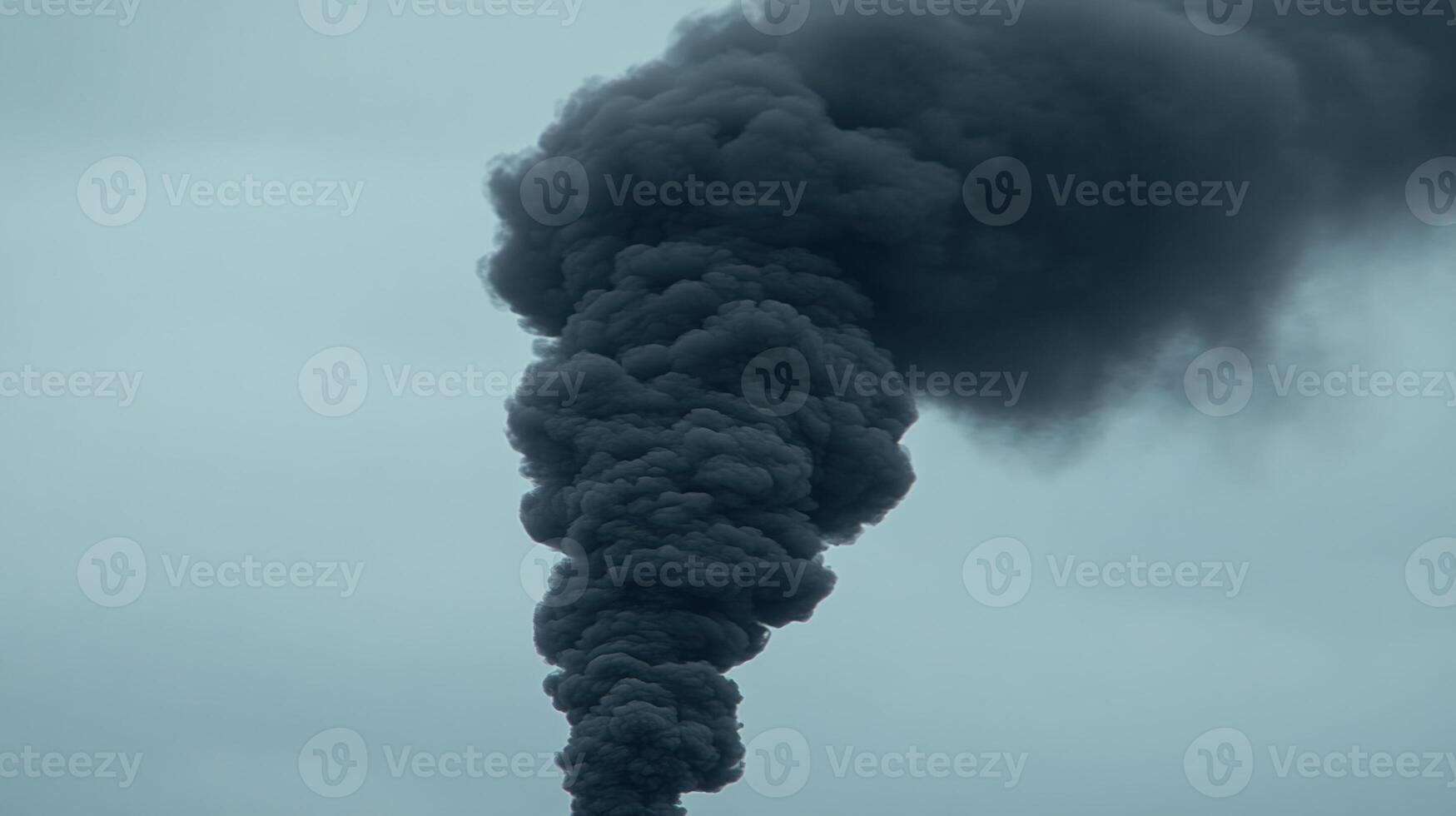 A thick column of dark smoke rises dramatically against the gray sky from a fire at an industrial site photo