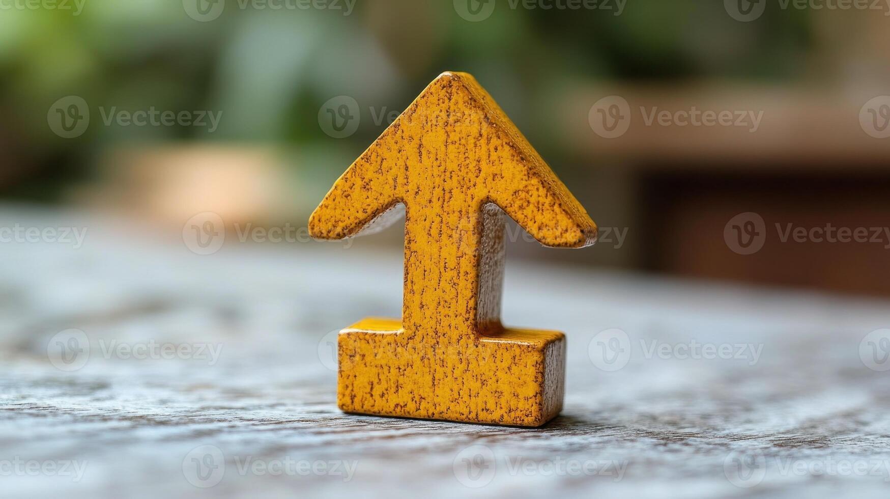 A bright yellow wooden arrow stands upright on a rustic wooden table, surrounded by greenery photo