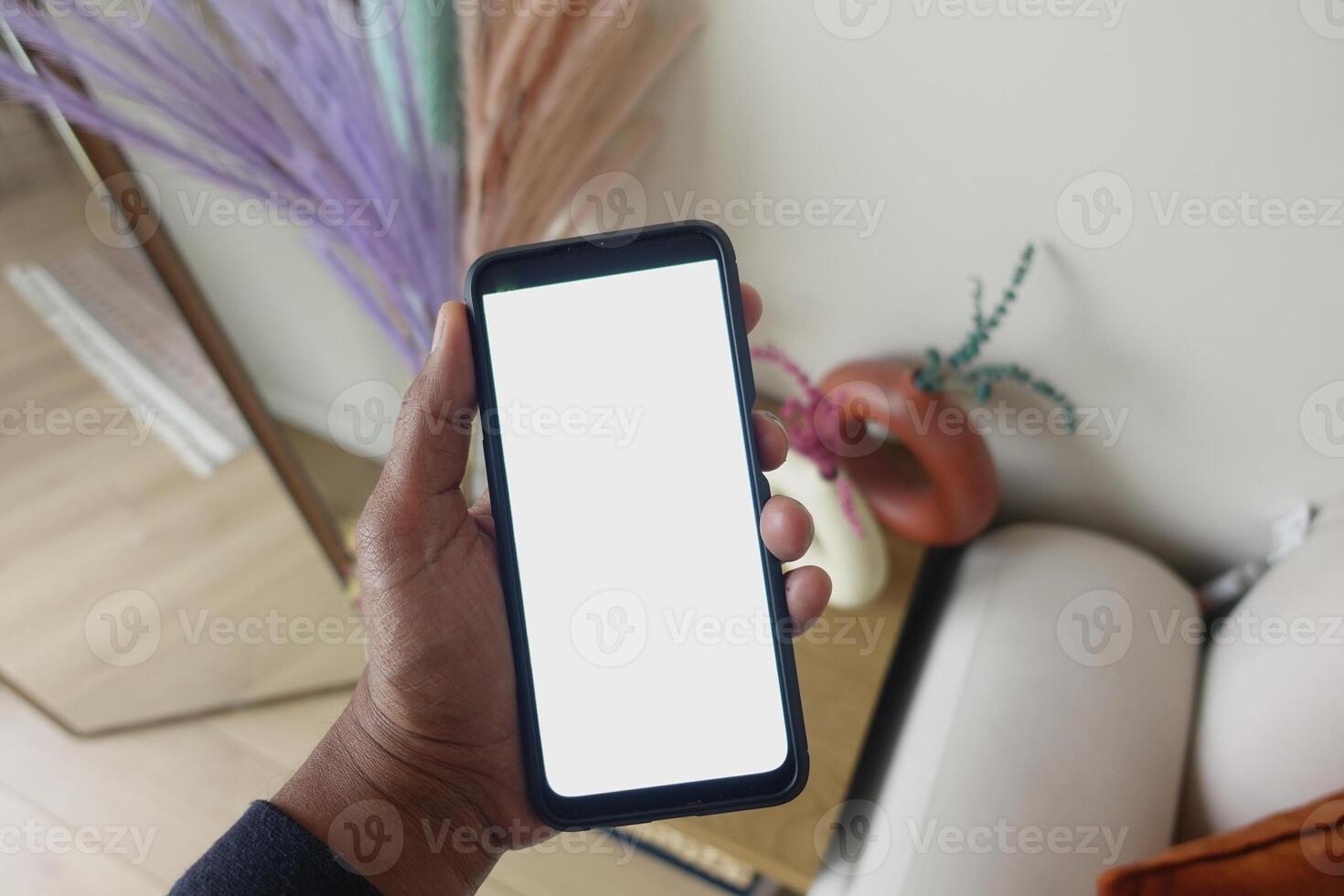 A hand holds a smartphone with a blank screen in a cozy setting photo
