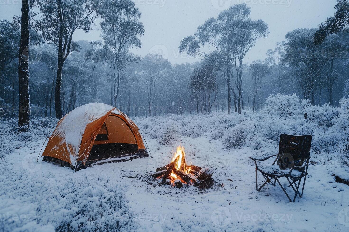 Camping tent glowing in snowy woods at dusk with burning campfire photo
