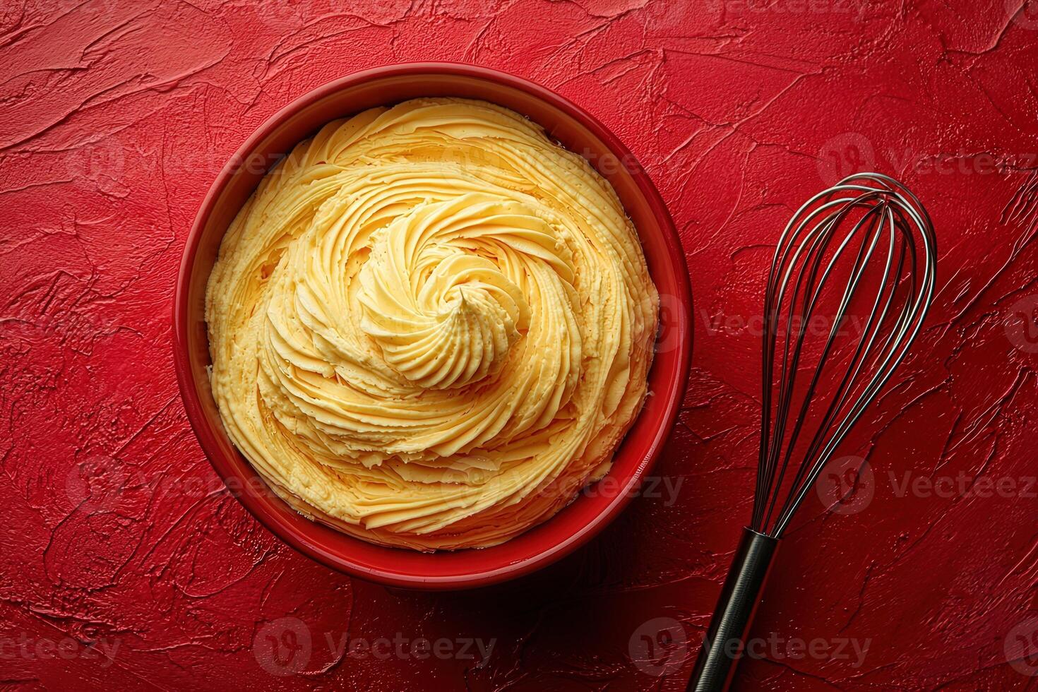 Creamy buttercream frosting is swirled beautifully in a red bowl, accompanied by a metal whisk. This delightful icing is perfect for cakes and cupcakes, adding a rich flavor and texture. photo