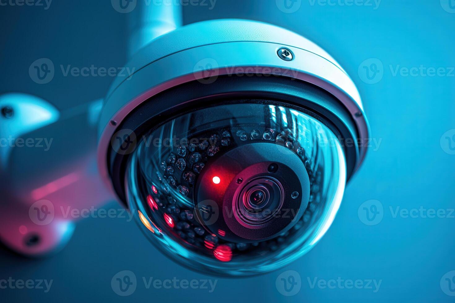 A detailed view of a security camera mounted on a wall captures the urban landscape at night, illuminated by blue and red lighting. The camera is actively monitoring its surroundings. photo