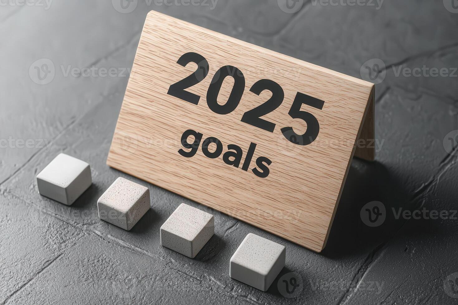 A wooden sign displays the year 2025 along with the word goals. Next to it are four gray blocks, symbolizing the steps or milestones towards achieving these goals, on a textured surface. photo