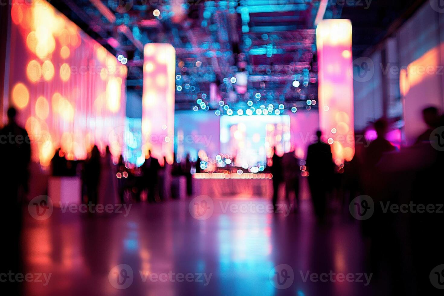 Vibrant lights illuminate a busy event space filled with guests mingling and enjoying the atmosphere. Colorful pillars and glowing backdrops enhance the lively scene. photo