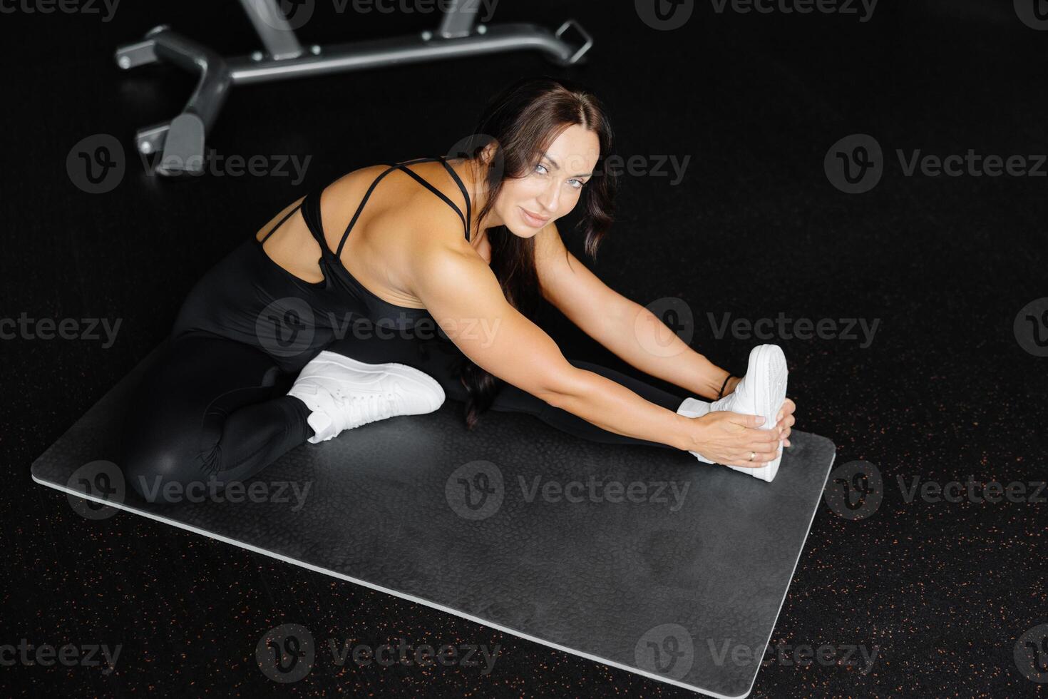 Woman is stretching body in gym. portrait and sport preparation. Young woman is stretching her leg in gym photo
