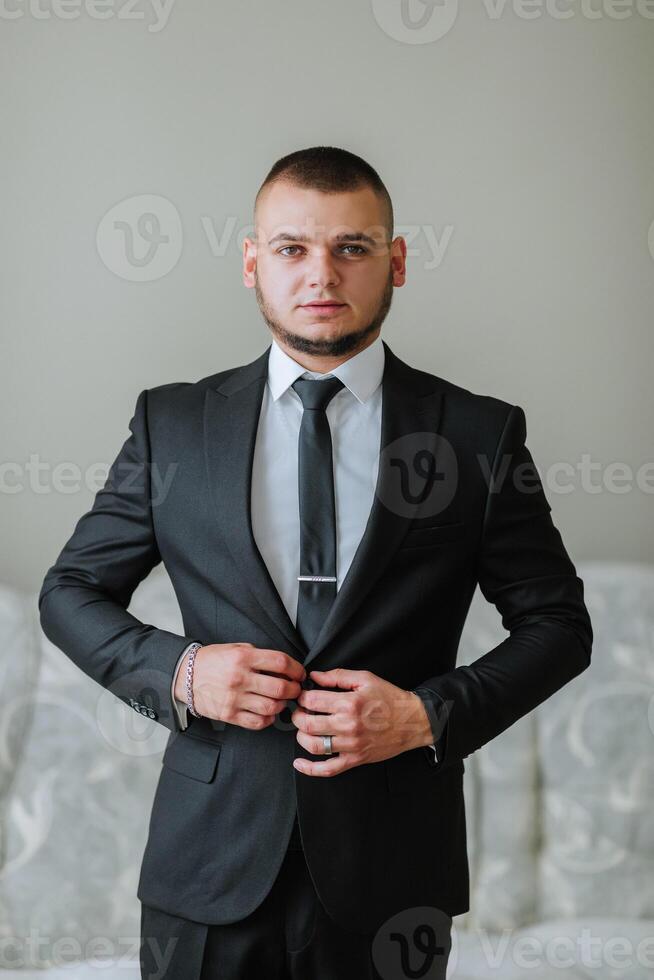 A man in a suit and tie is standing in front of a bed photo