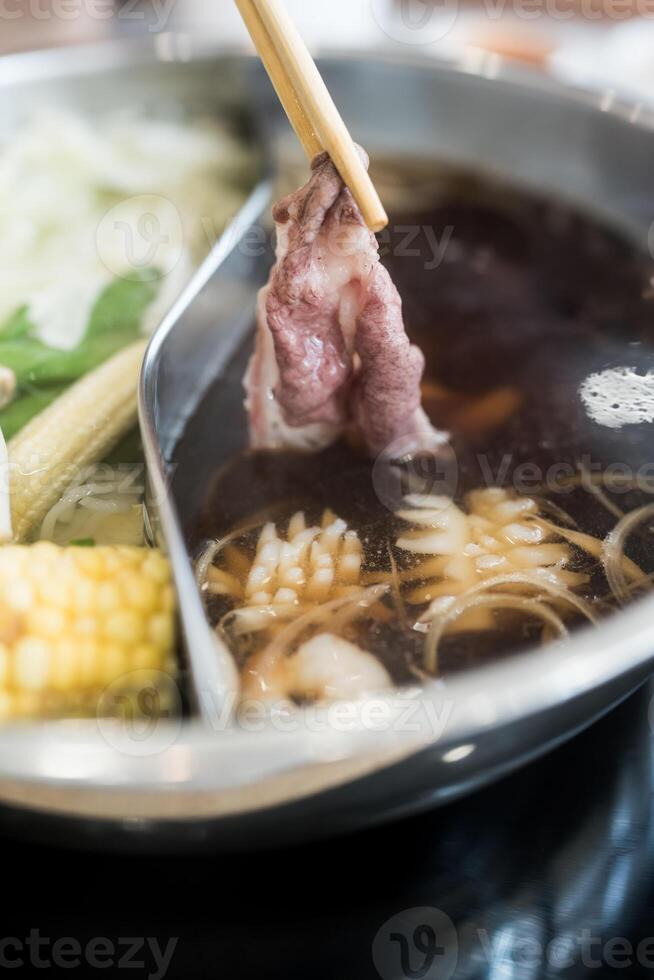 Man holding slice beef out from hot pot shabu shoyu soup base. photo