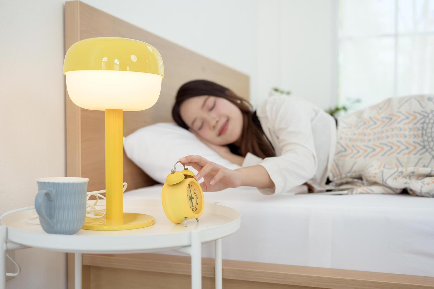 Sleeping asian woman turning off alarm on clock while being Waken up in the morning photo
