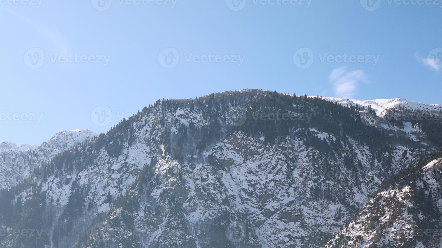 Snowy Mountain Ridge with Evergreen Trees with Sunlight in Day and a Clear Blue Sky in Kalam, Pakistan photo