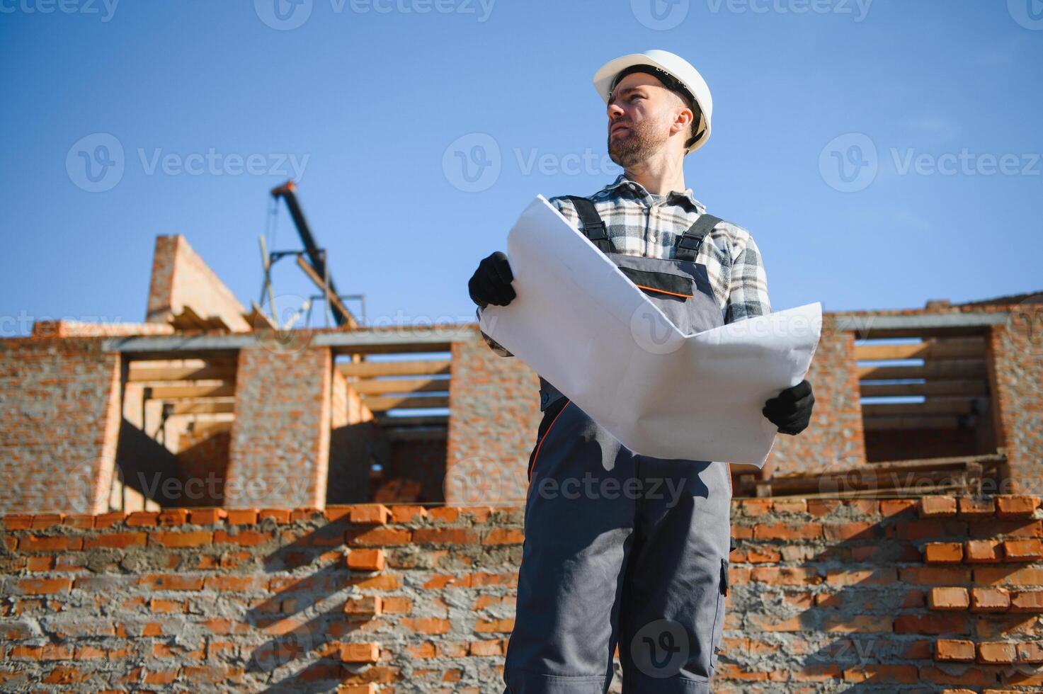 An architect or engineer on the construction of brick houses holds the construction plan in his hands and checks the execution of the work photo