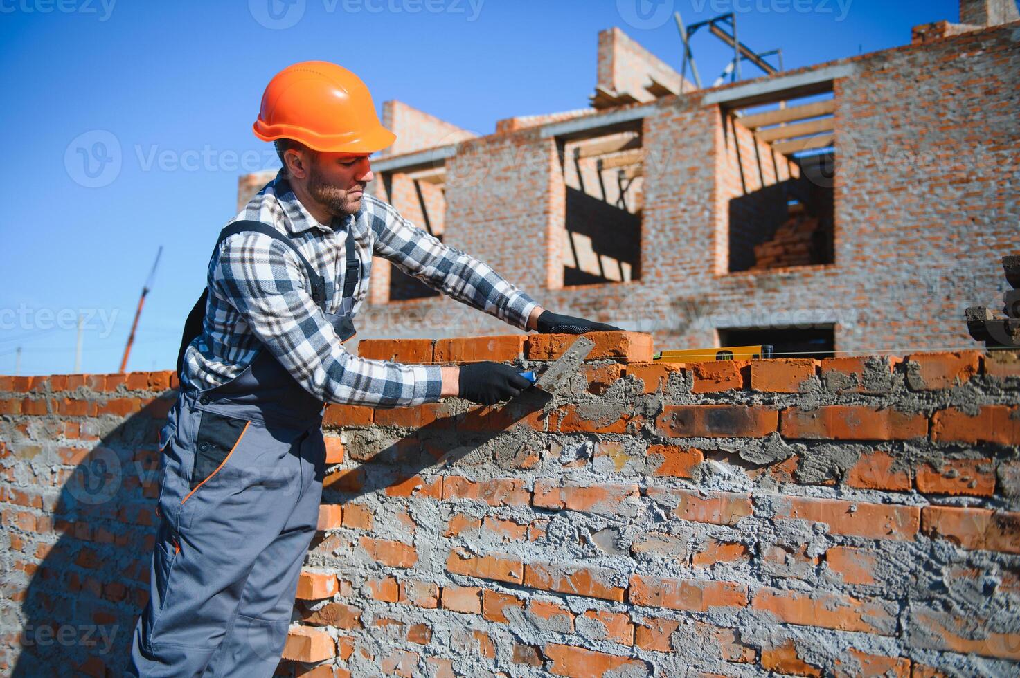 Bricklayer industrial worker installing brick masonry on exterior wall with trowel putty knife photo