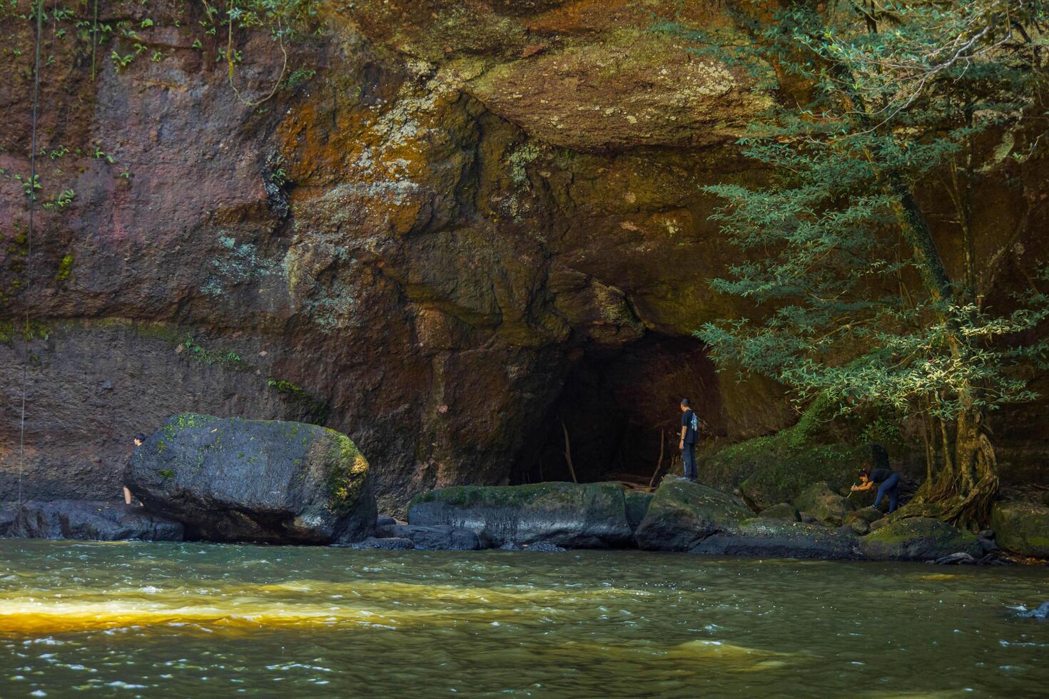 Serene river flowing through a forest with a cave nestled by the water. National park, Thailand. photo