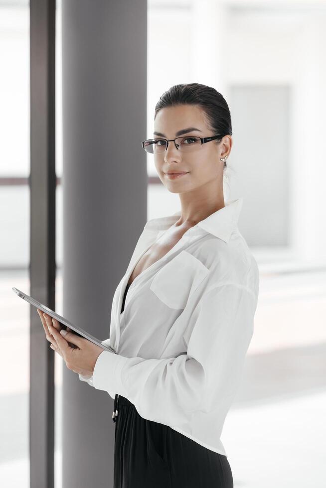 Young multi-ethnic female in formalwear using tablet computer, watching online presentation. Startup project. Professional consulting colleague expert. Confident focused businesswoman wearing glasses photo