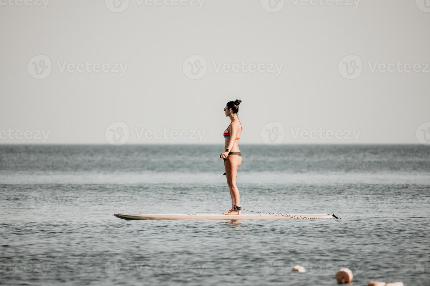 Sea woman sup. Silhouette of happy middle aged tanned woman in rainbow bikini, surfing on SUP board, confident paddling through water surface. Idyllic sunset. Active lifestyle at sea or river. photo