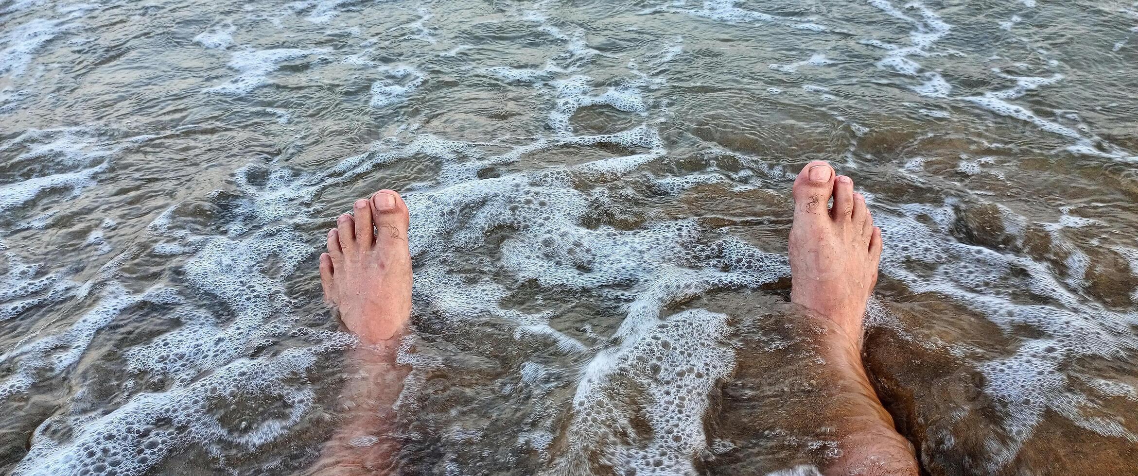 Male legs in water with wave on beach of Mediterranean sea coast photo