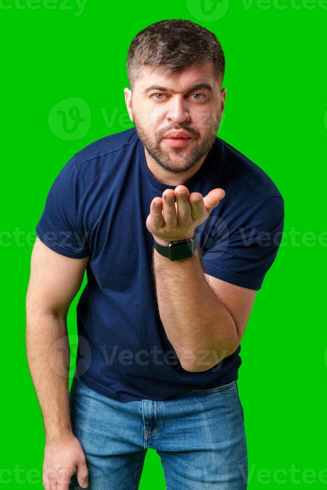 A man blowing a kiss while standing against a bright green backdrop in a casual outfit photo