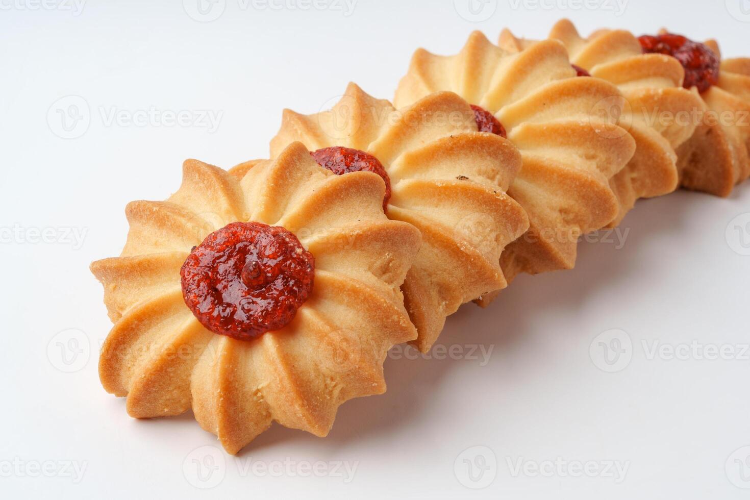Sweet cookie blossoms topped with red fruit preserves arranged in a decorative pattern on a white surface photo