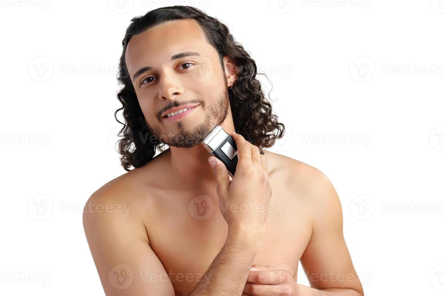 A young man with curly hair grooming his beard using an electric trimmer photo