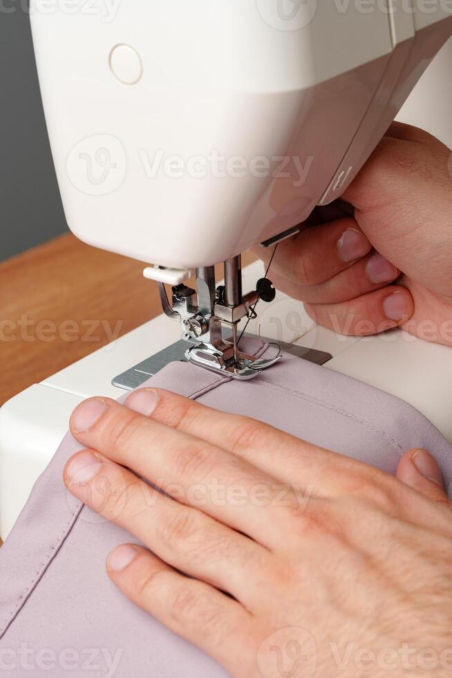 Hands sewing fabric using a sewing machine on a wooden table in a well-lit workspace photo