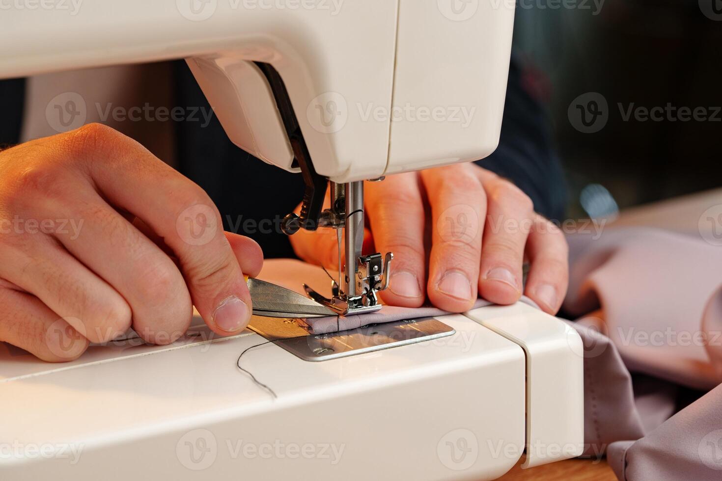 Hands sewing fabric using a sewing machine on a wooden table in a well-lit workspace photo
