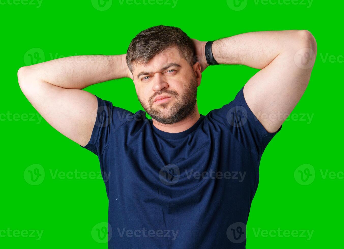 A man poses confidently with his hands behind his head against a bright green background photo