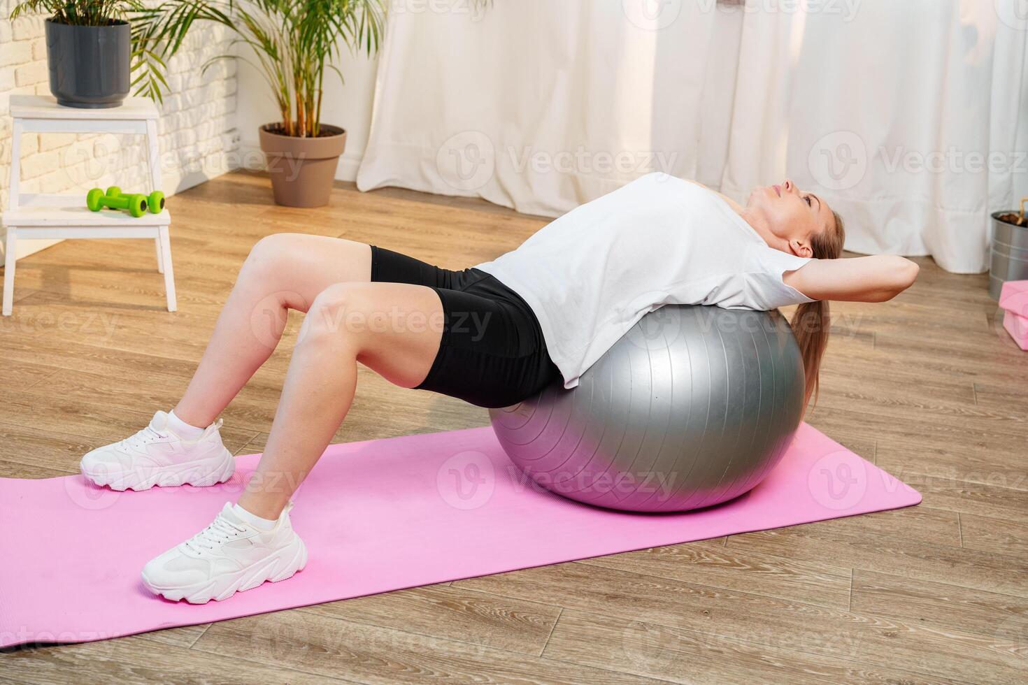 Young woman exercising on a stability ball in a bright room with plants photo