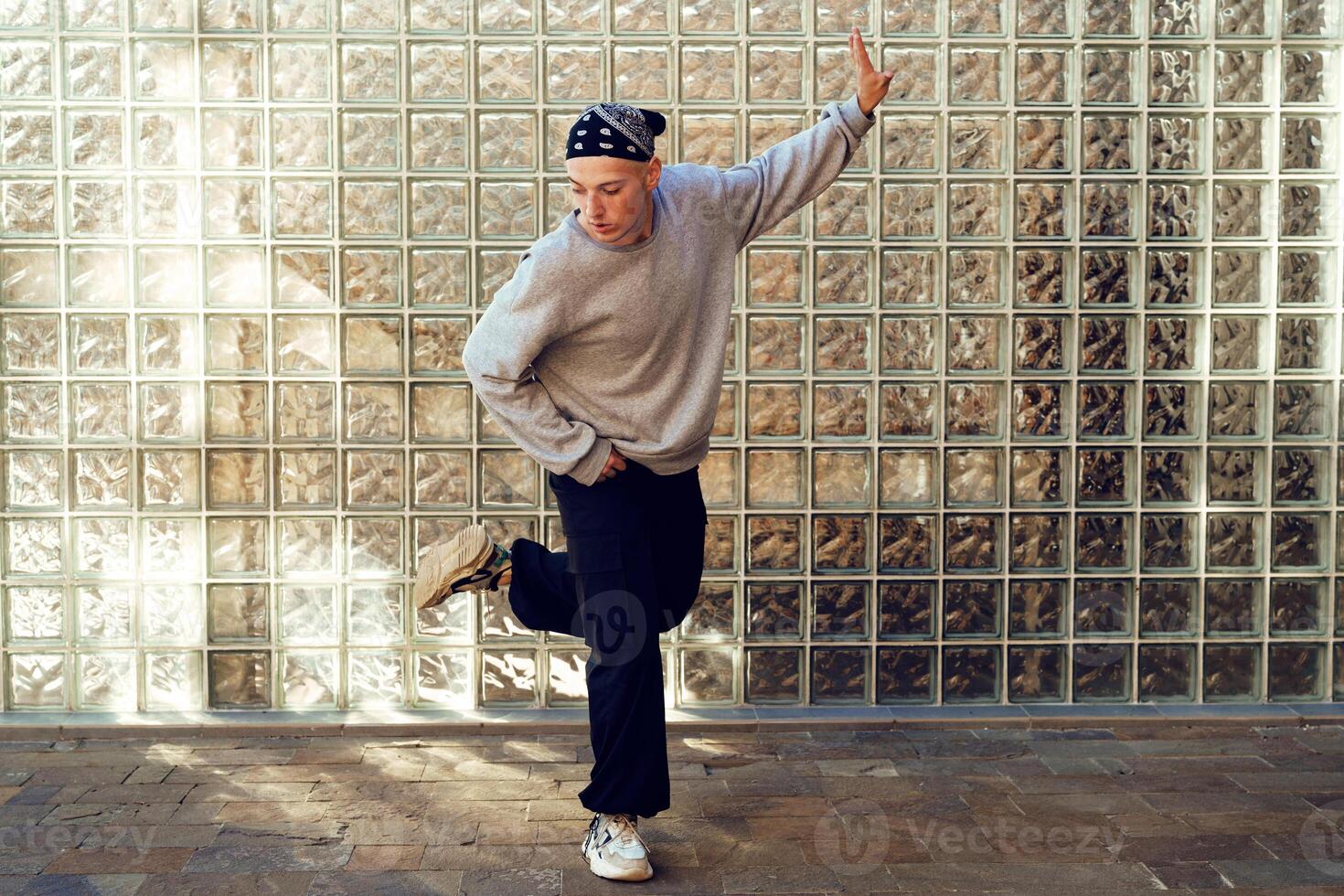 A young man performs a dance move in front of a brick wall photo