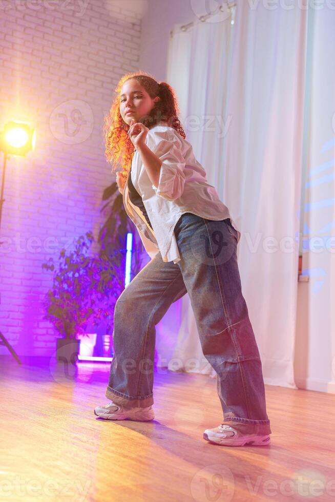 A young woman with curly red hair dances in a studio lit with colored lights photo