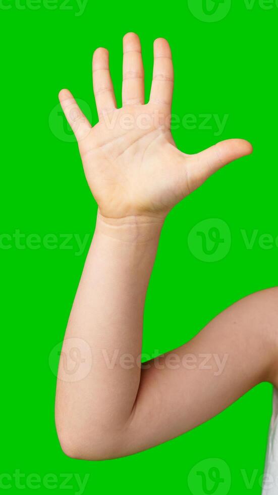 A child's hand raised in greeting against a bright green background photo