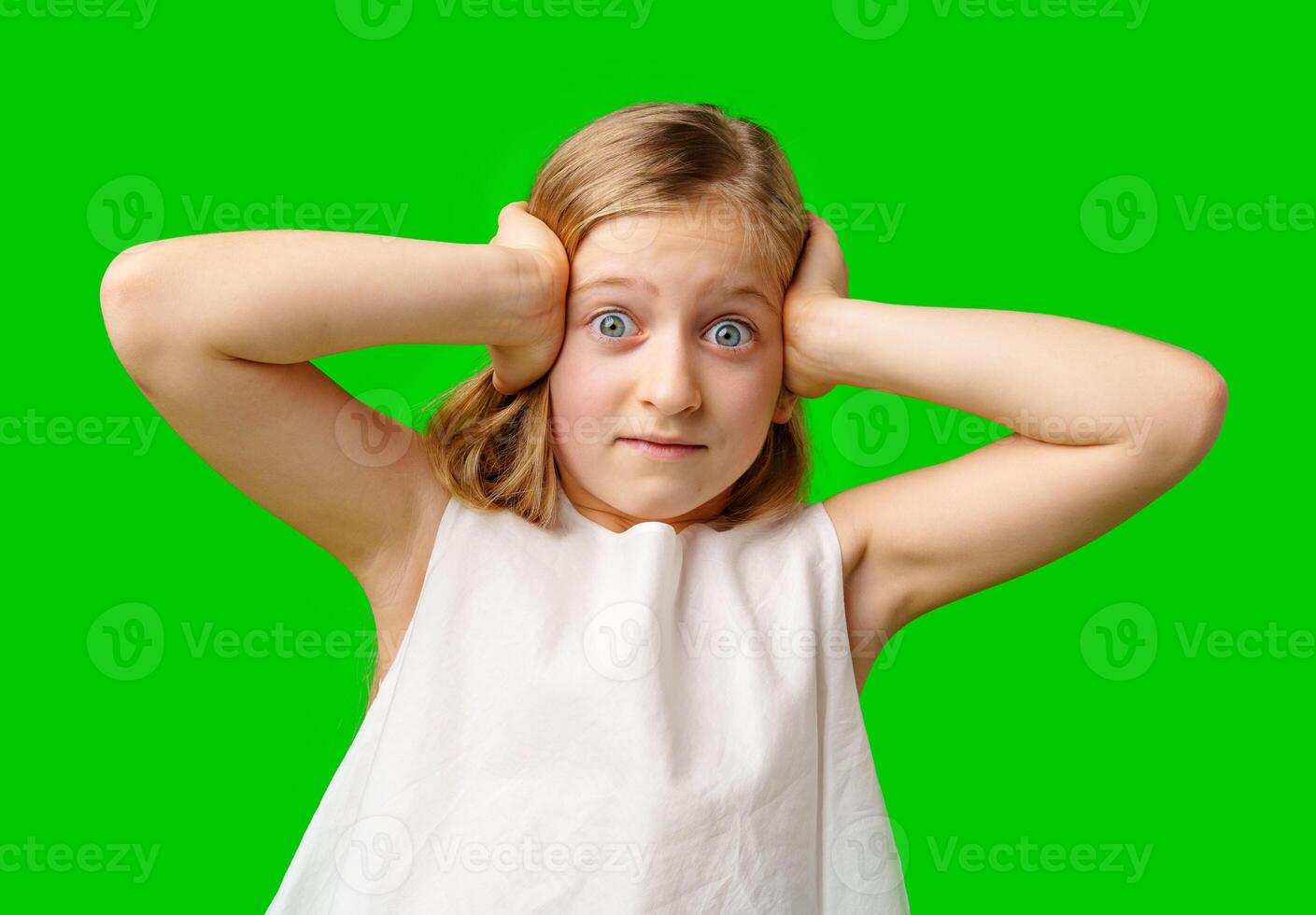 A young girl covers her ears with a worried expression in front of a bright green background photo