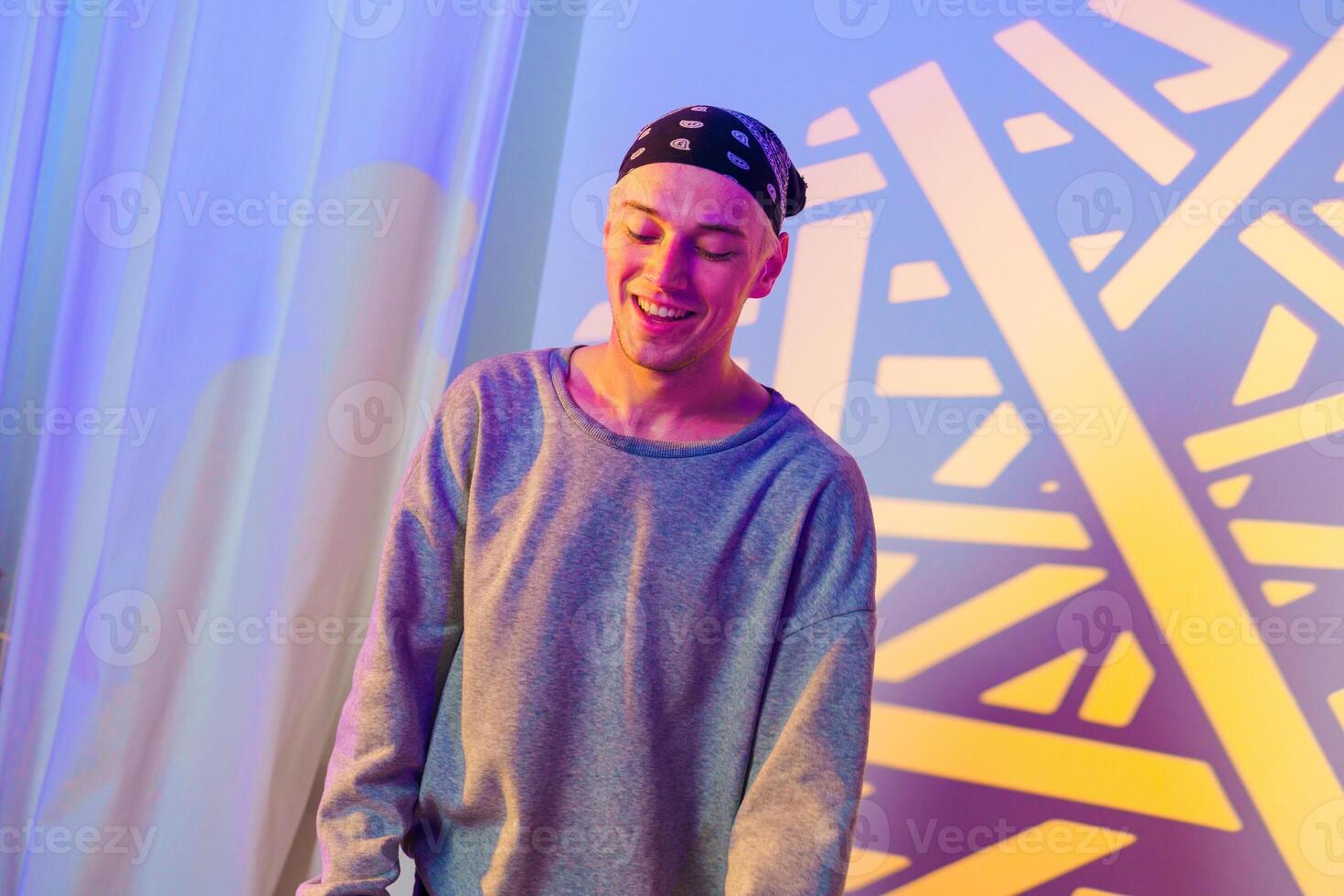 A young man wearing a bandana smiles in front of a colorful backdrop photo