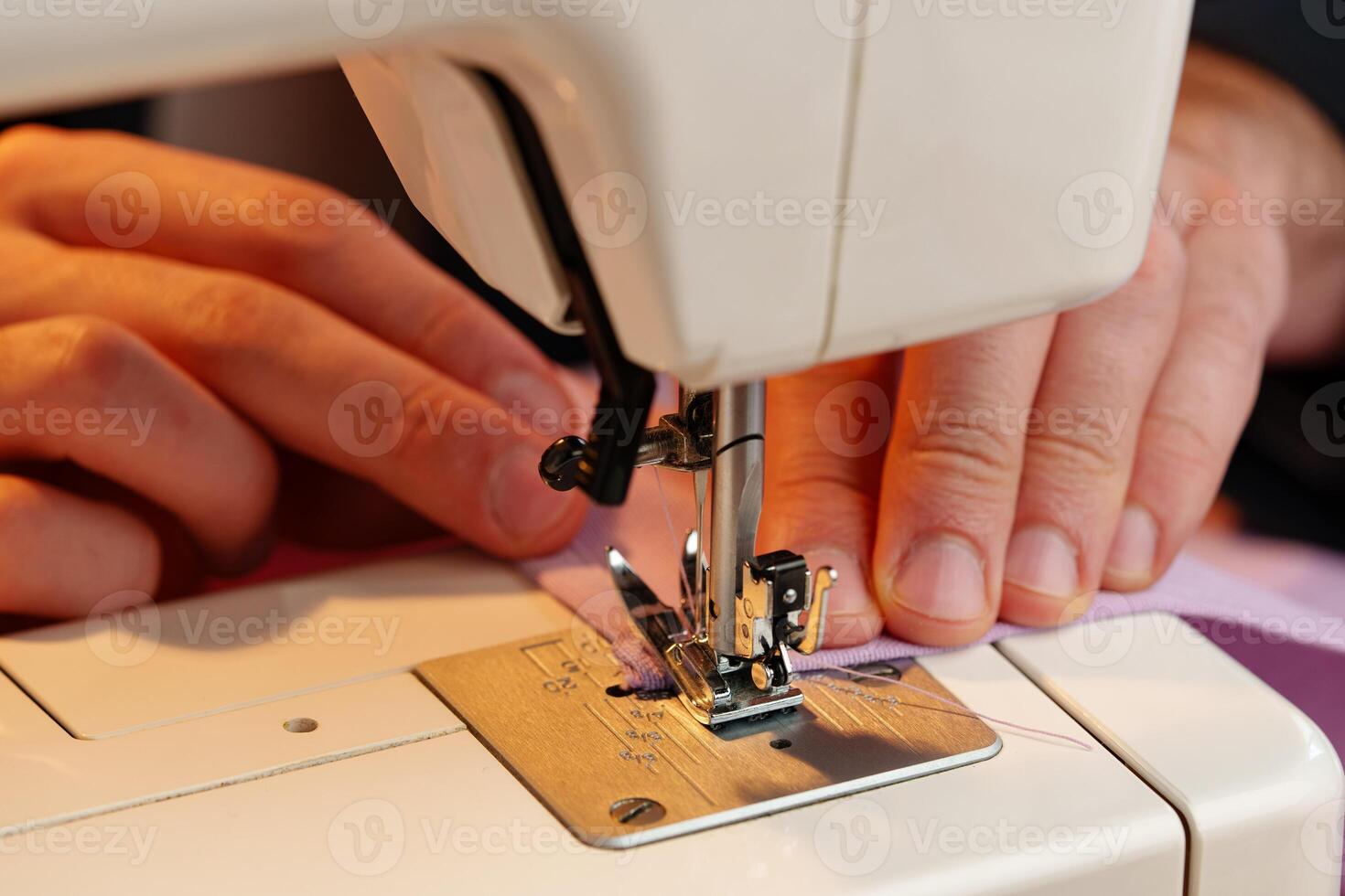 Hands sewing fabric using a sewing machine on a wooden table in a well-lit workspace photo