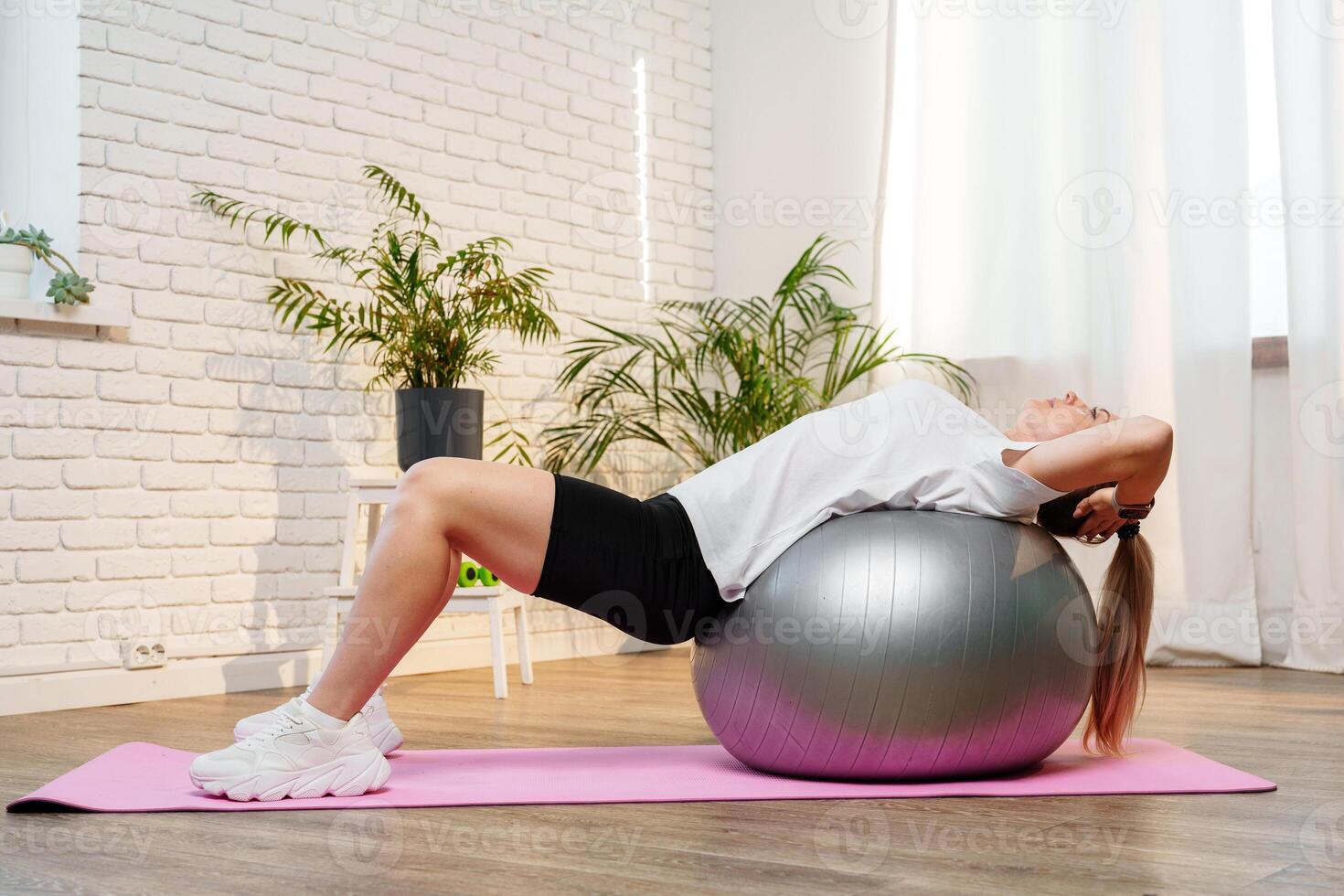 Young woman exercising on a stability ball in a bright room with plants photo
