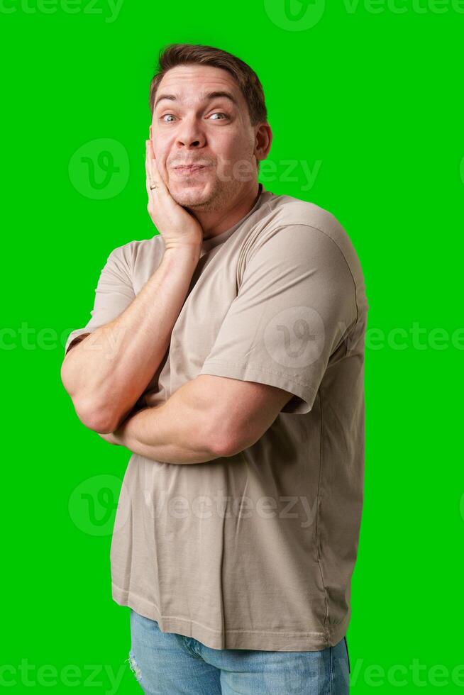 Man posing thoughtfully with hand on chin in casual attire against a bright green background photo