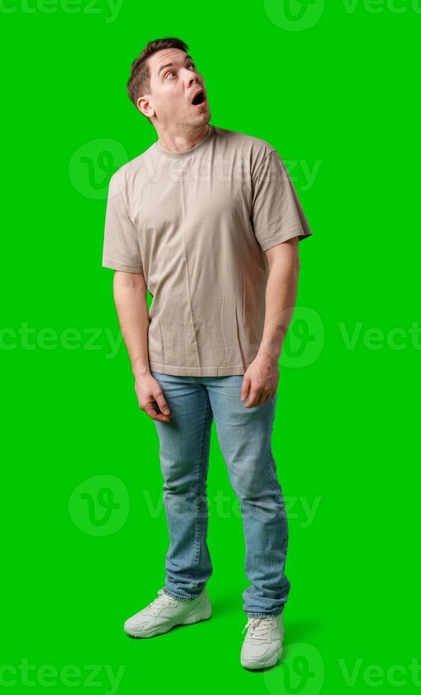 A surprised man stands in front of a bright green screen, expressing shock with his mouth open photo