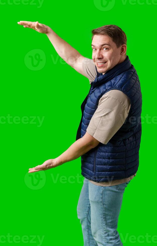 Man in a navy vest gestures enthusiastically toward a green screen photo