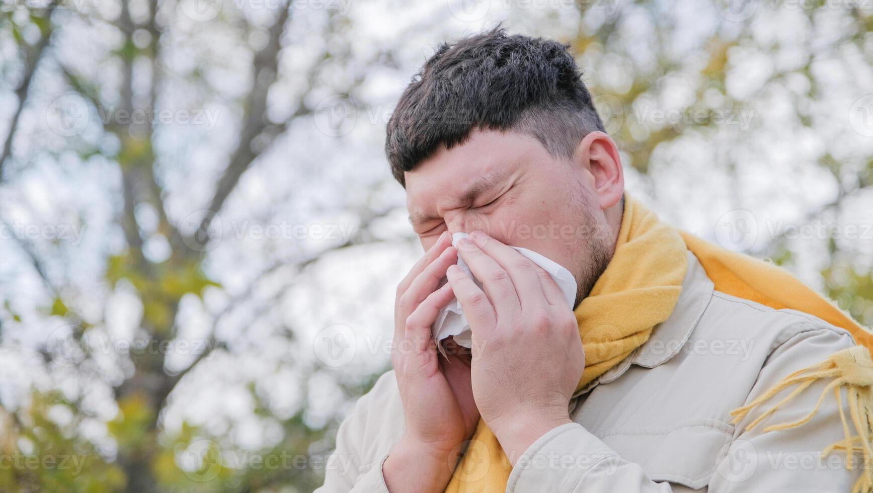 young man enjoying autumn days breathing fresh air using tissue to wipe nose photo