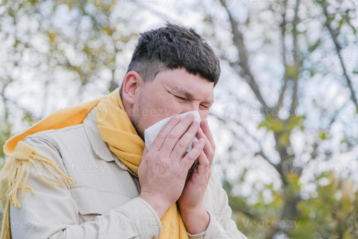 young man enjoying autumn days breathing fresh air using tissue to wipe nose photo