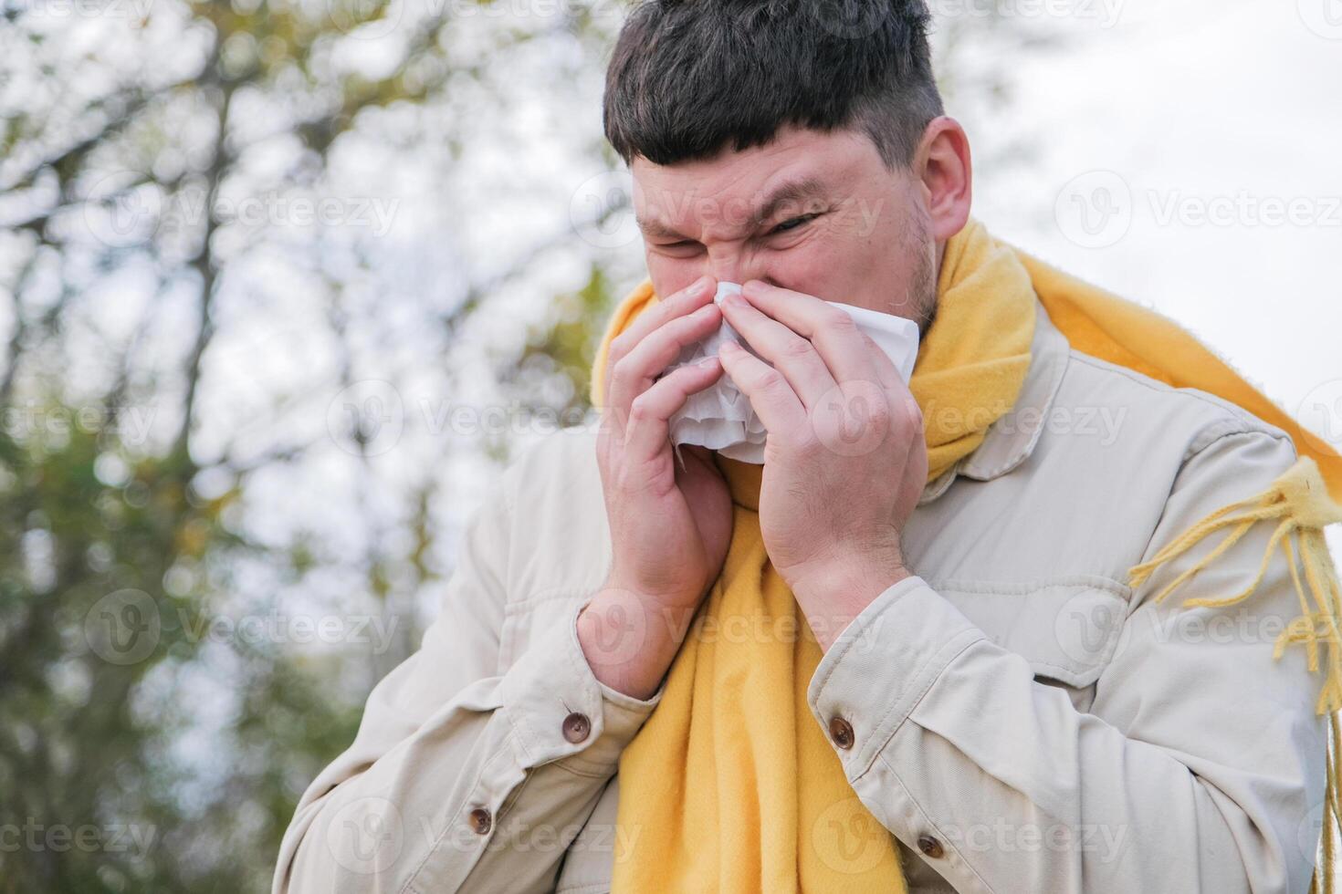 young man enjoying autumn days breathing fresh air using tissue to wipe nose photo