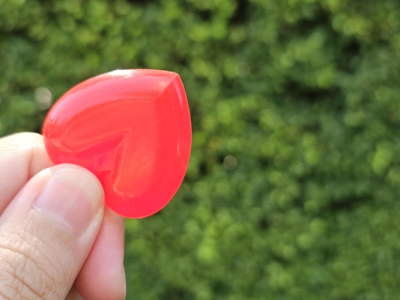 Hand holding red plastic heart shaped spoon with copy space, Blurred background, Valentine Day Theme photo