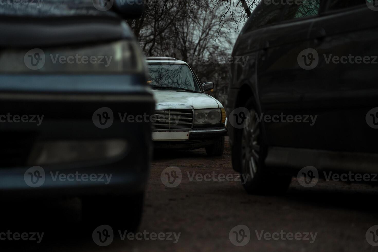 An old, abandoned, German, white car is parked in the evening photo