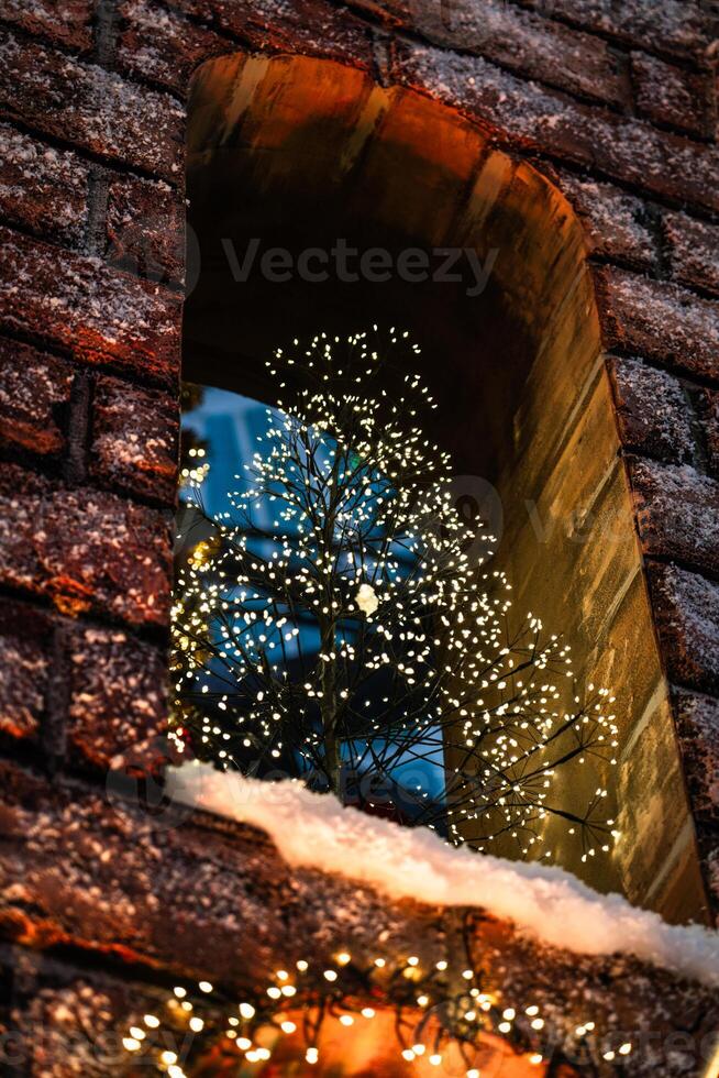 A small Christmas tree stands on the window of a brick building. New Year photo