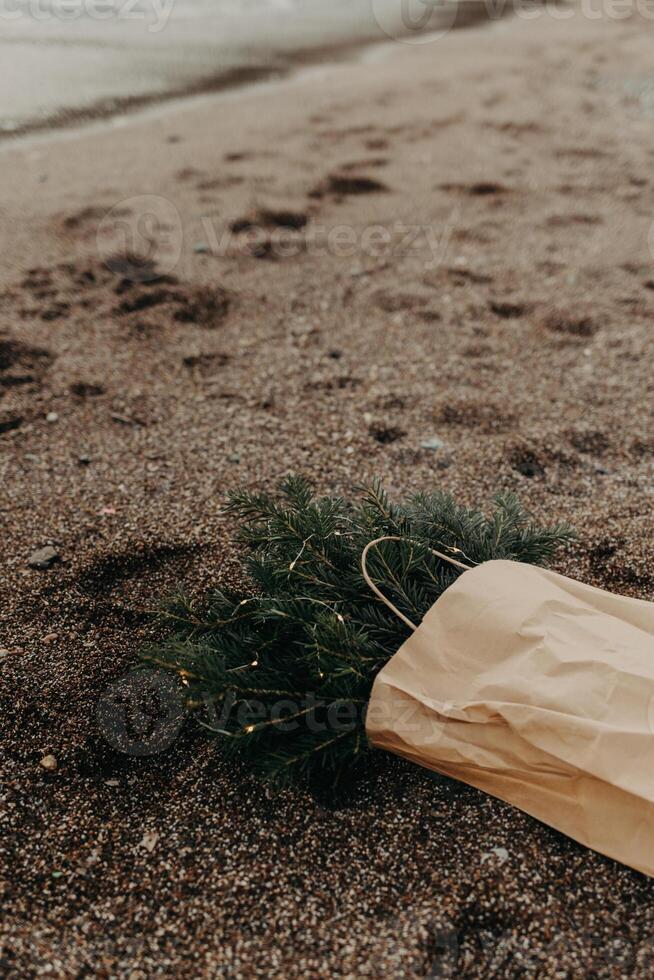 Craft Bag with Spruce branches with Christmas lights laying on a sand on the beach. photo