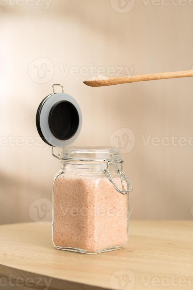 A jar of Himalayan salt sits on a table, with a wooden spoon scooping some. photo