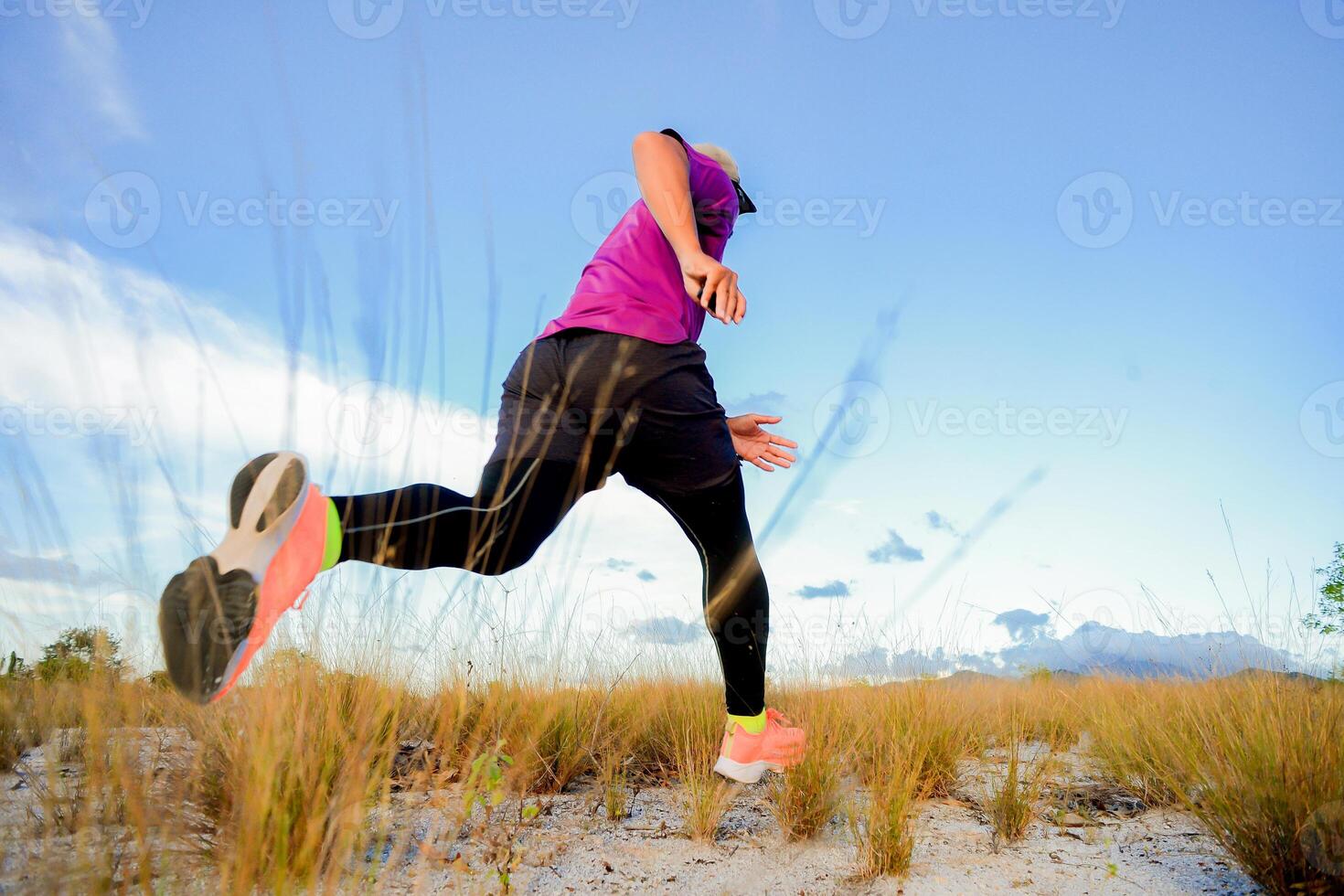 Dynamic Low-Angle Shot of a Runner in Vibrant Athletic Wear Sprinting Through a Grassy Field Under a Clear Blue Sky photo