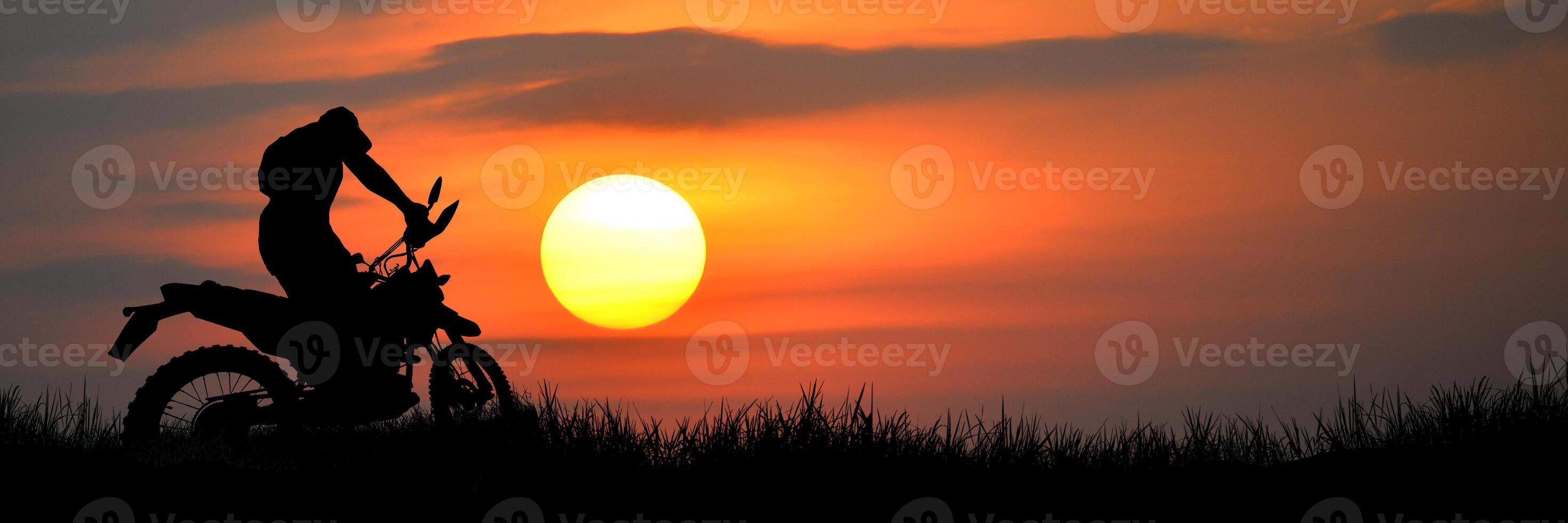 Silhouette of Motorcyclist Against Vibrant Sunset Sky with Dramatic Orange and Yellow Hues in Tranquil Outdoor Landscape photo