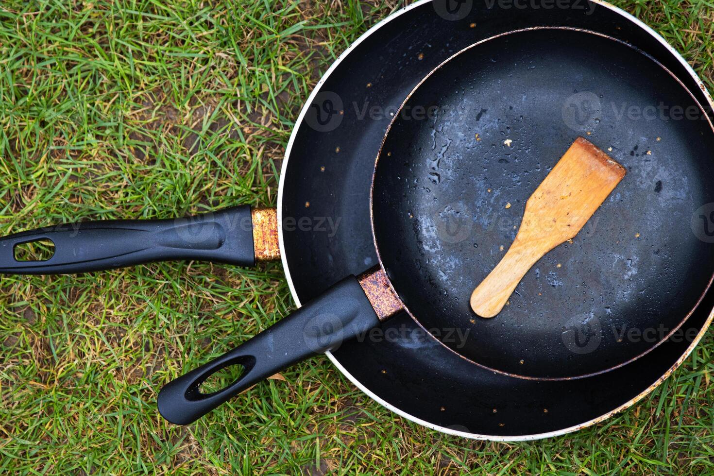 Top view of two black frying pans with a wooden spatula on a green grass, symbolizing camping lifestyle, outdoor cooking, minimalism, and rustic living concepts. photo