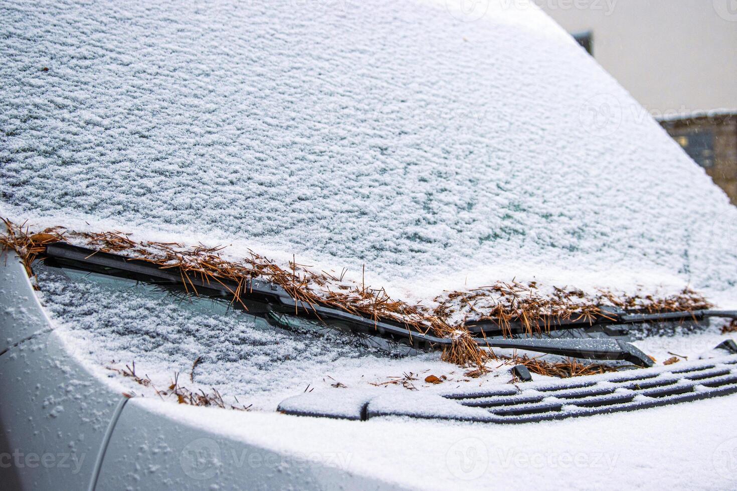 Snow covered frosty car windshield with leaves on wipers. Winter traffic in snowfall. Challenging driving conditions, icy roads, and seasonal weather impacts on transportation. Copy space photo